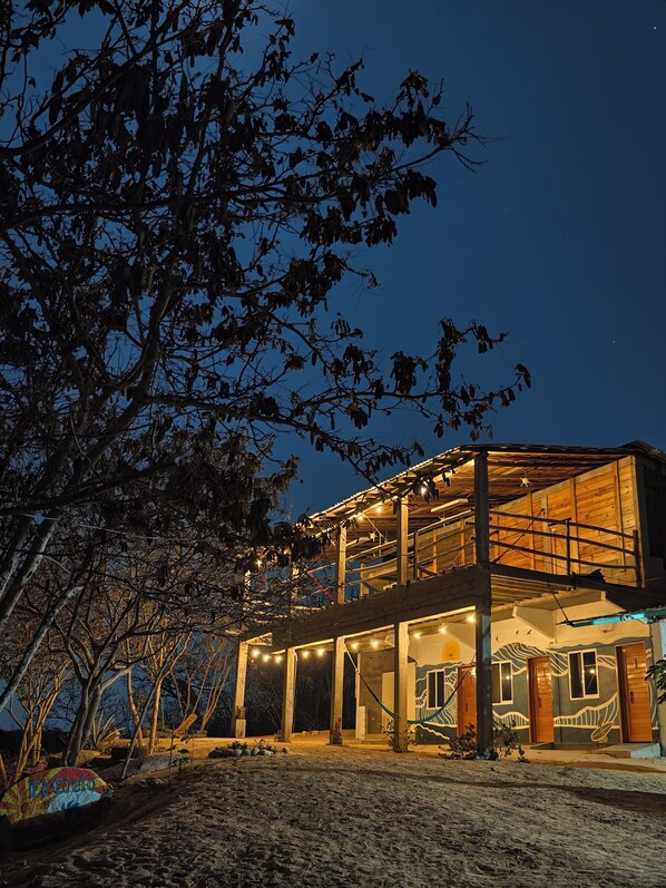 A two-story building with a balcony, large windows, and a sandy ground.