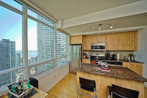 A modern kitchen with granite countertops, wooden cabinets, and a large window offering a city view. - Fairview Downtown (Toronto)