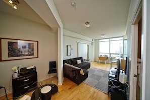 A modern living room with a dark sofa, a glass coffee table, and a framed picture on the wall. - Fairview Downtown (Toronto)
