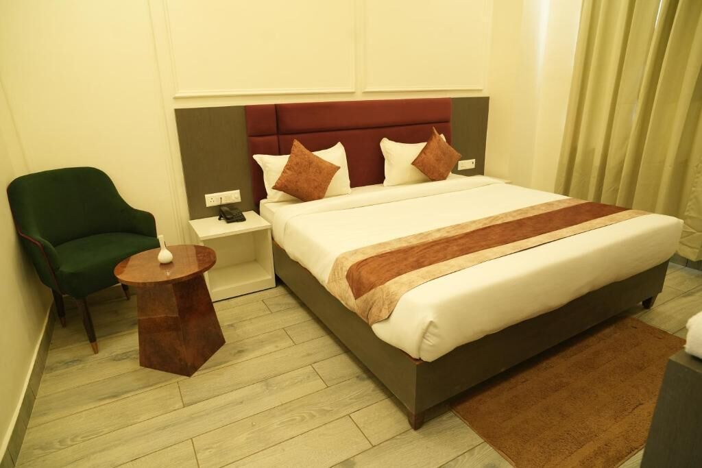 A hotel room with a bed, a green armchair, a bedside table, and a nightstand.
