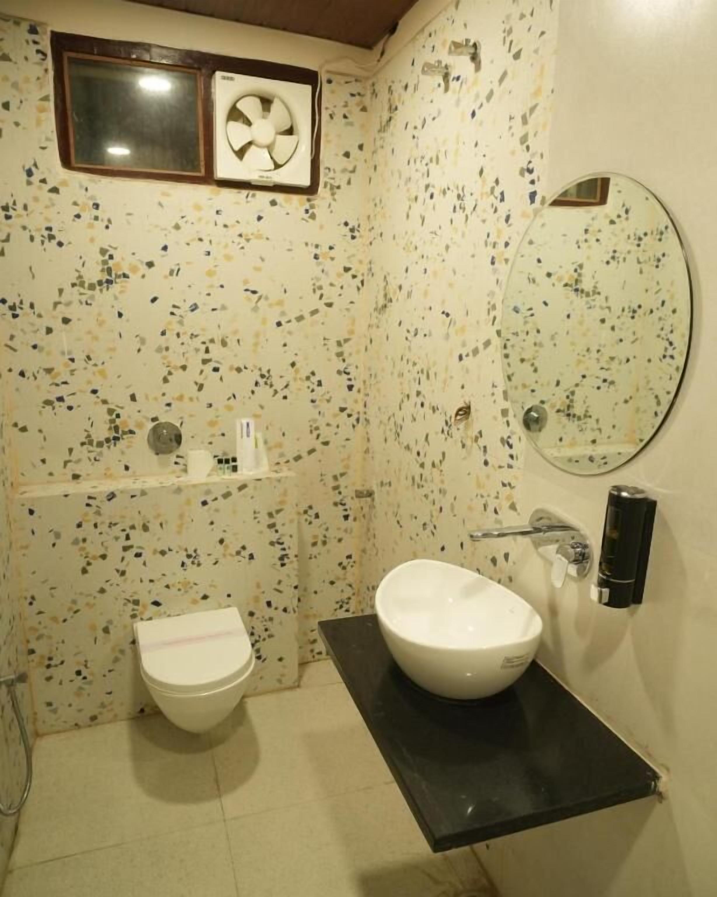 Une salle de bain équipée de toilettes, d’un lavabo, d’un miroir et d’un ventilateur fixé au mur.