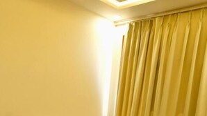 Un sofá amarillo, dos sillones y una mesita de centro en una habitación con piso estampado color verde y una cortina.