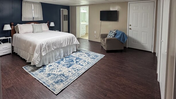 A bedroom with a bed, nightstands, a TV, a chair, and a door.