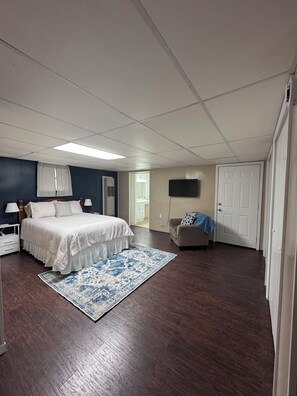 Une chambre à coucher avec un lit, des tables de chevet, un téléviseur, une chaise et une porte.