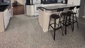 A modern kitchen with white cabinets, a black countertop, and a bar area with stools.