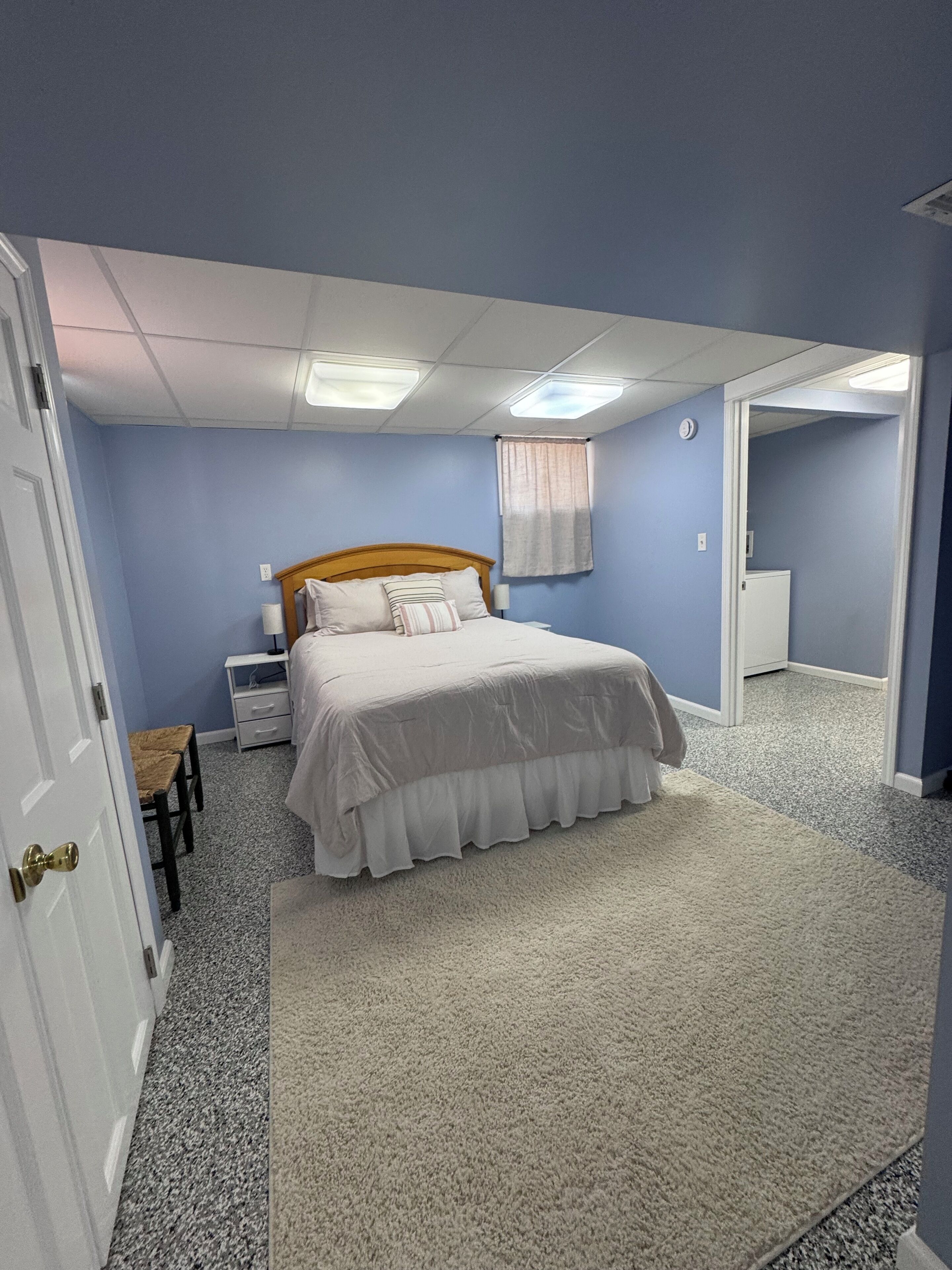 A bedroom with a bed, a nightstand, a chair, a door, and a carpeted floor.