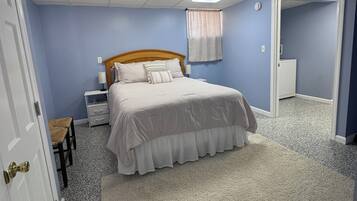 A bedroom with a bed, a nightstand, a chair, a door, and a carpeted floor.