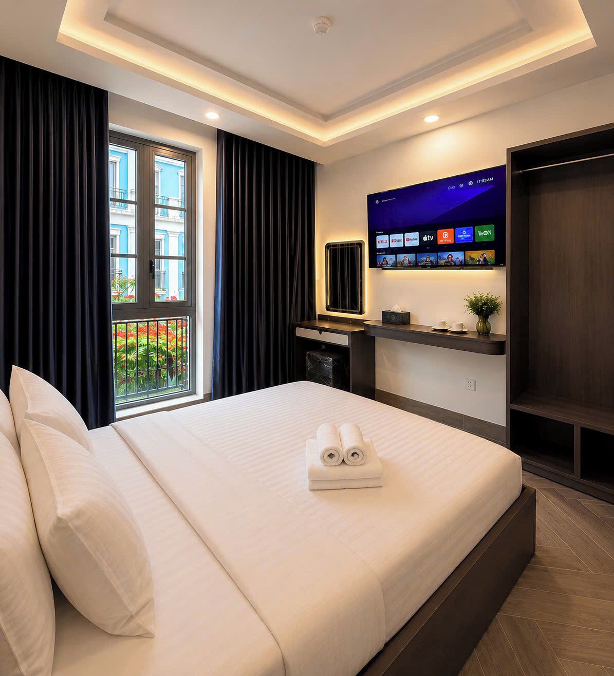 Ein Hotelzimmer mit Bett, Wand-Fernseher, Schreibtisch mit Stuhl und einem Vorhangfenster.