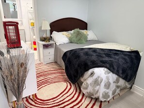 A bedroom with a bed, bedside table, lamp, and a red telephone booth.