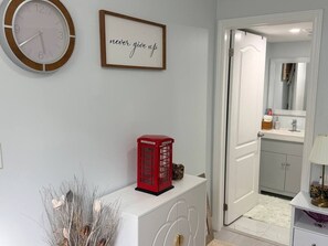 A room with a white console, a red telephone booth, a framed motivational quote, and a mirror in the background.