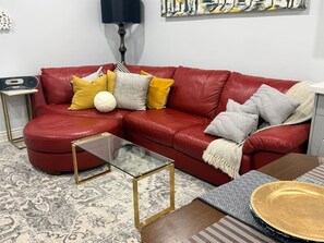 A red leather sofa with a glass coffee table and a patterned rug. - Parkview - A Cozy Gem (Mississauga)