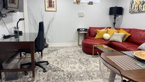 Un salon avec un canapé rouge, une table basse en verre, un tapis à motifs et un bureau avec une chaise.