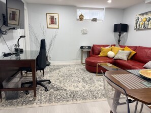 A living room with a red sofa, a glass coffee table, a patterned rug, and a desk with a chair.