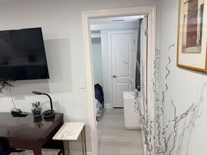 Una habitación con escritorio, televisión de pantalla plana, puerta blanca y un cuadro en la pared.