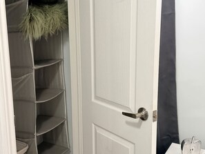 A white door with a metal handle, a grey shelving unit with a fluffy green item on top, and a dark curtain partially visible. - Parkview - A Cozy Gem (Mississauga)