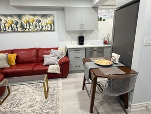 Una sala de estar moderna con un sofá rojo, una mesa de comedor con sillas, una zona de cocina con armarios y un cuadro grande en la pared.