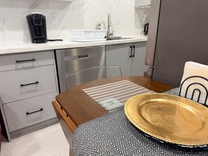 Una cocina moderna con cafetera, pileta y comedor con mantel estampado y un sombrero.