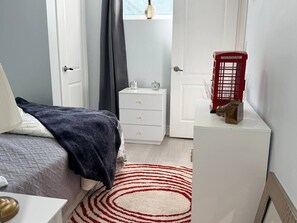 A bedroom with a bed, a white dresser, a red telephone booth, and a window with a view. - Parkview - A Cozy Gem (Mississauga)