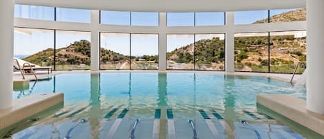 A large indoor swimming pool with clear views of a hilly landscape through large windows.