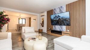 Una sala de estar moderna con un televisor de pantalla plana, sofás blancos, una mesa de centro y una pared de acento de madera.