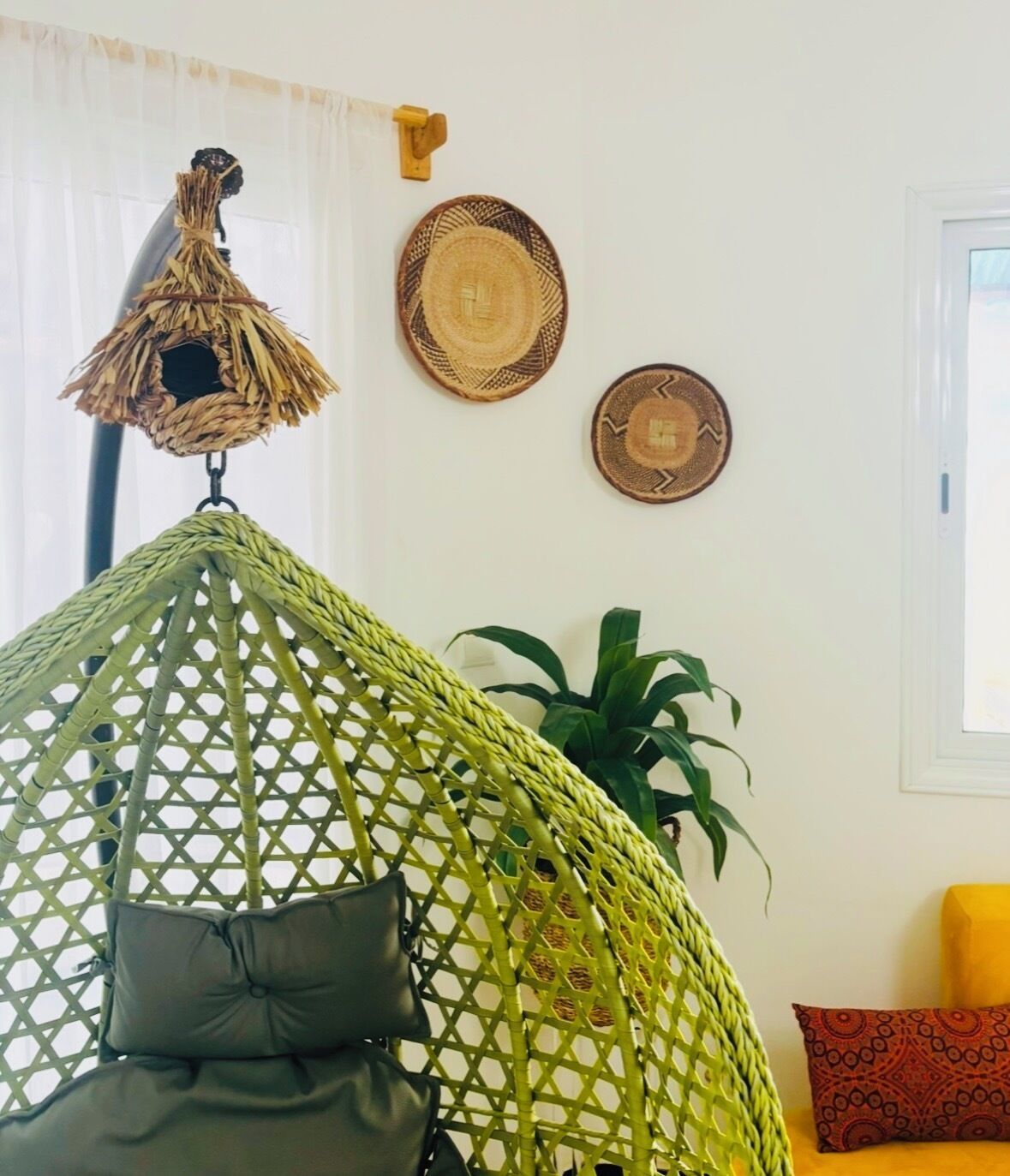 Una habitación con una silla colgante, una planta en maceta y dos tapices tejidos.