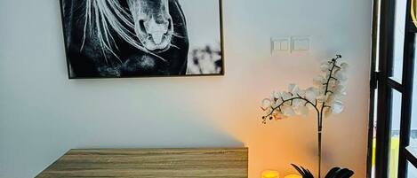 A room with a desk, a framed horse portrait, a potted plant, and a window.