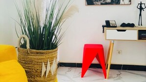 A room with a yellow sofa, a wicker basket with plants, a red stool, a desk with a telephone, and a framed horse portrait on the wall. - 2-bedroom apartment in charming Dakar with AC and comfort (Dakar)