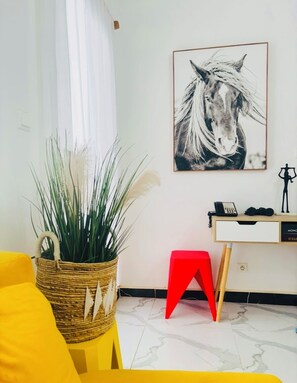 A room with a yellow sofa, a wicker basket with plants, a red stool, a desk with a telephone, and a framed horse portrait on the wall. - 2-bedroom apartment in charming Dakar with AC and comfort (Dakar)