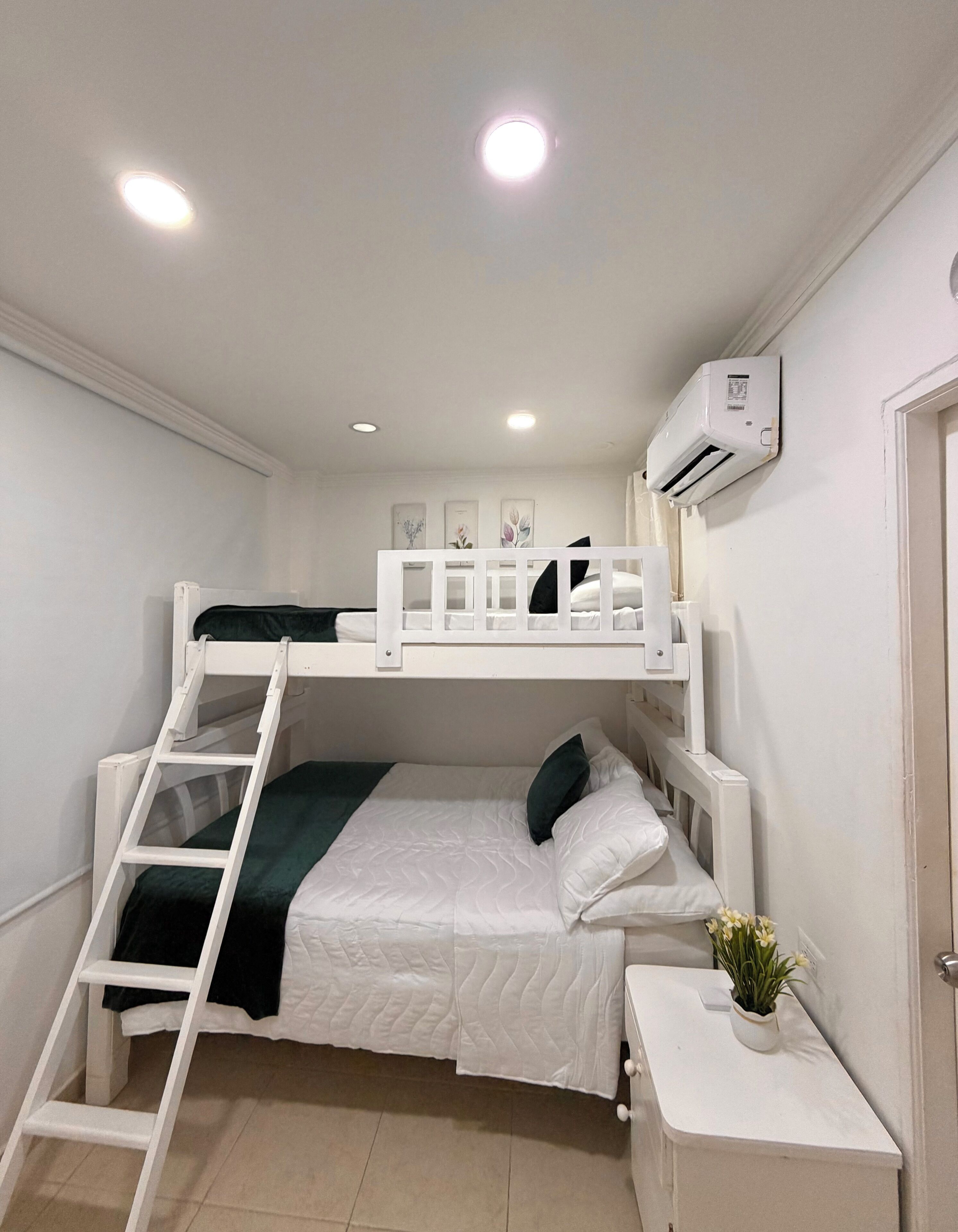 Une chambre avec un lit superposé, une échelle, des murs blancs et un appareil de climatisation.