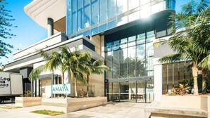 Un edificio moderno con fachada de vidrio, palmeras y un cartel que dice 'AMAYA'.