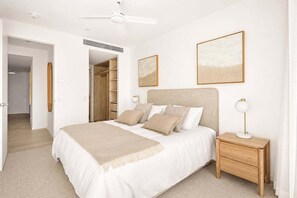 Un dormitorio con cama, mesitas de noche, ventilador de techo y vestidor.