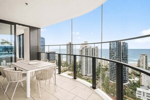 A balcony with a dining table and chairs, overlooking a coastal cityscape with high-rise buildings and the ocean. - Amaya Coastal Luxe | Pool & Panoramic Views (Gold Coast)