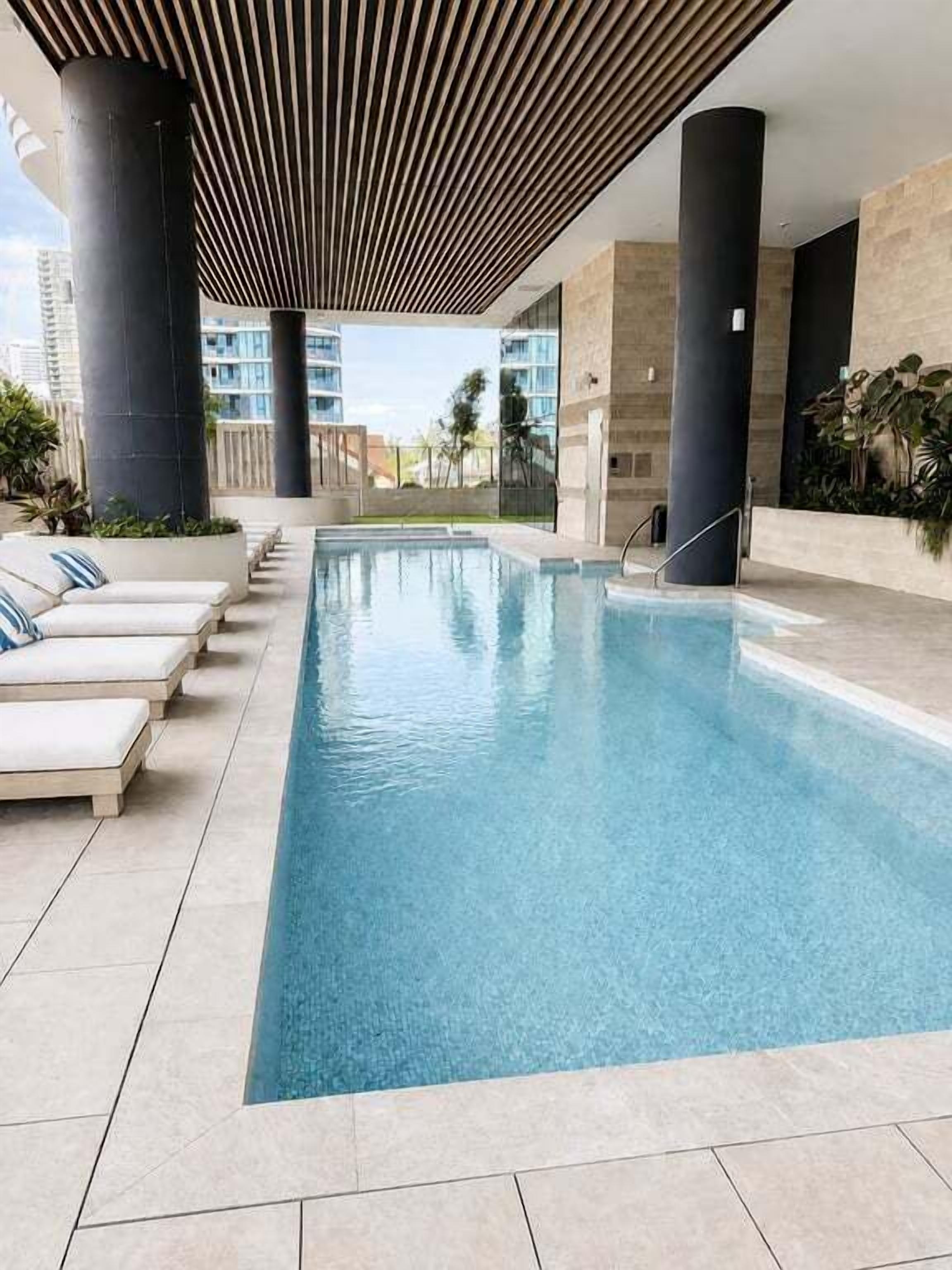 Ein Schwimmbecken mit Liegestühlen, umgeben von moderner Architektur und Pflanzen.
