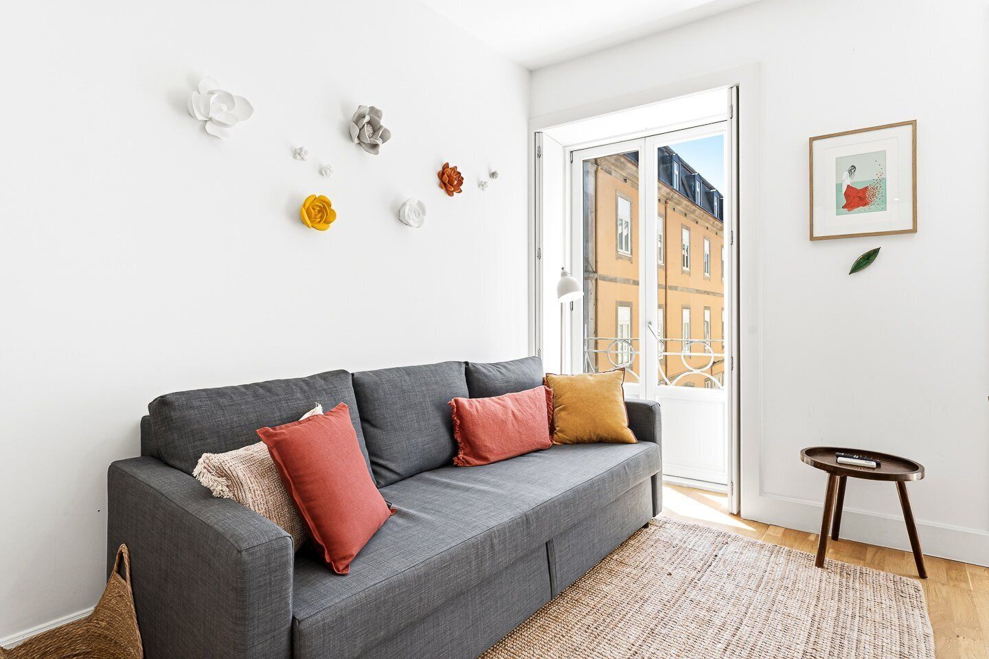 Un sofá gris con cojines rojos y beiges, un tapiz tejido y elementos decorativos en la pared.