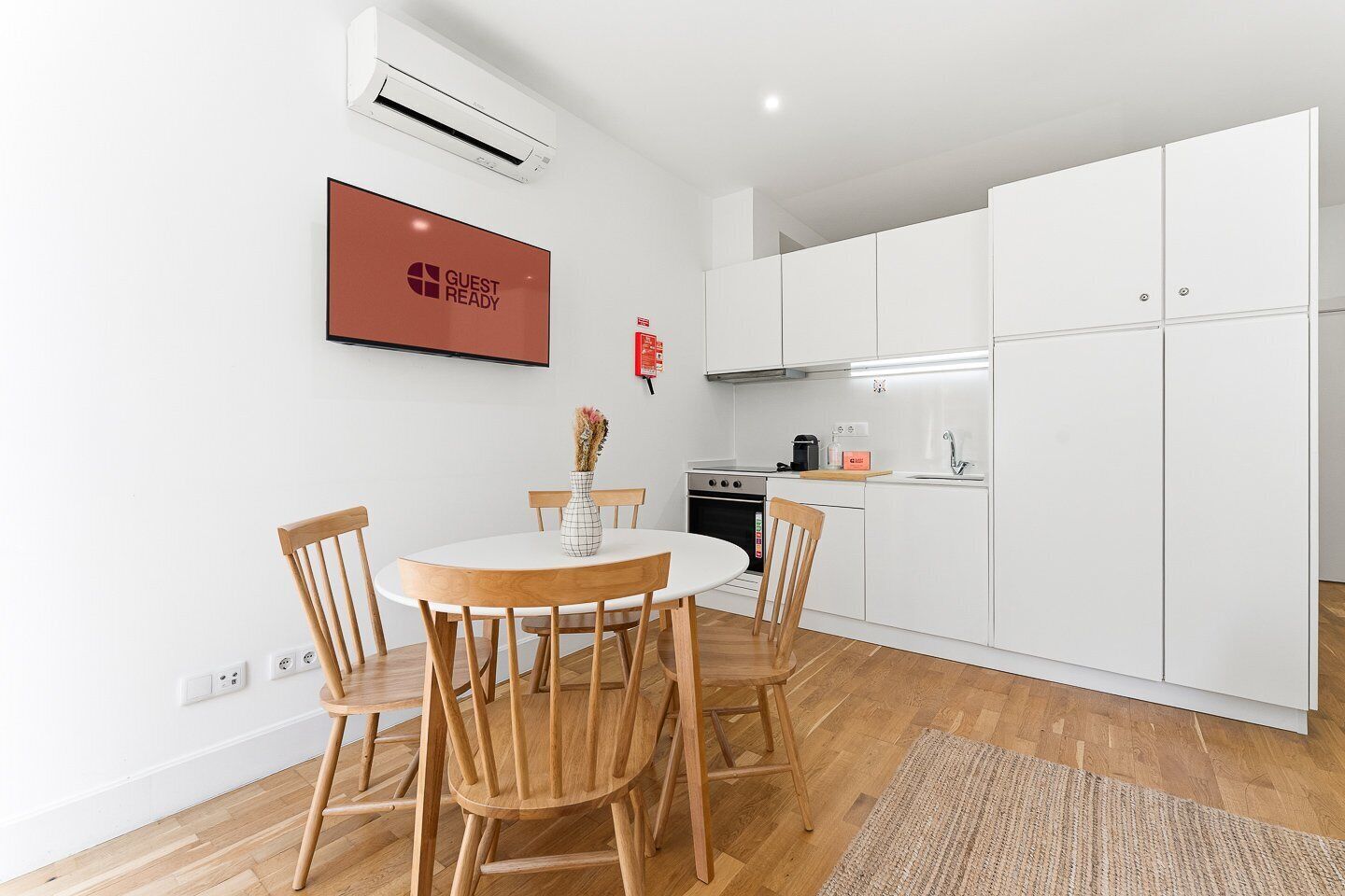 Una cocina moderna con gabinetes blancos, una mesa de comedor con sillas de madera y una pequeña isla con una cafetera.