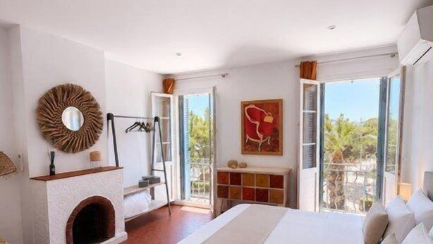 Ein Schlafzimmer mit einem großen Bett, einem Kamin, Blick durch eine Glastür und einem roten, abstrakten Gemälde.