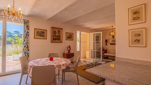 Uma sala de jantar ampla com uma mesa posta para quatro pessoas, um candelabro e vista para o exterior.
