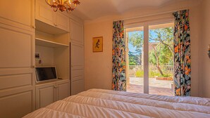 Quarto com cama, escrivaninha, lustre e vista por uma porta.