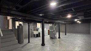 Un sótano con piso de concreto, vigas expuestas y una lavadora.