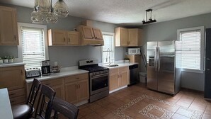 Una cocina con gabinetes de madera, estufa, refrigerador y un comedor con sillas.