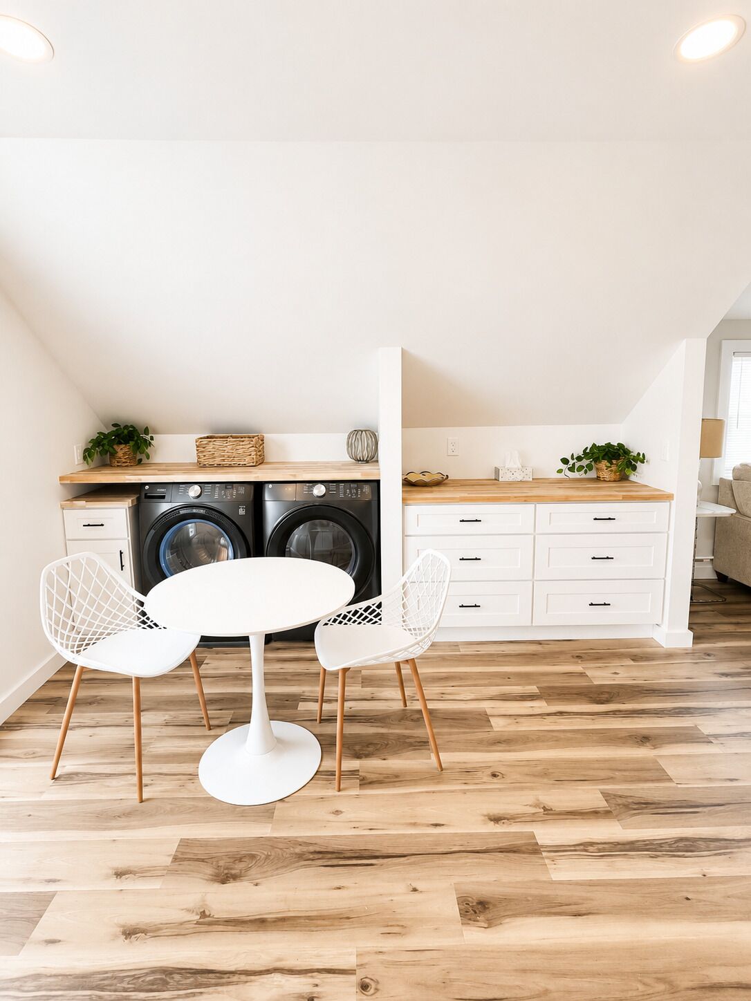 A compact kitchen with a washing machine, a dining table with chairs, and a white cabinet.