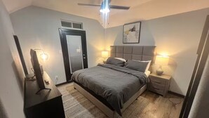 A bedroom with a bed, bedside tables, a ceiling fan, and a door. - Entire home in Houston central, Texas (Houston)