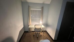 A small, sparsely furnished room with a desk, chair, and a window with blinds. - Entire home in Houston central, Texas (Houston)