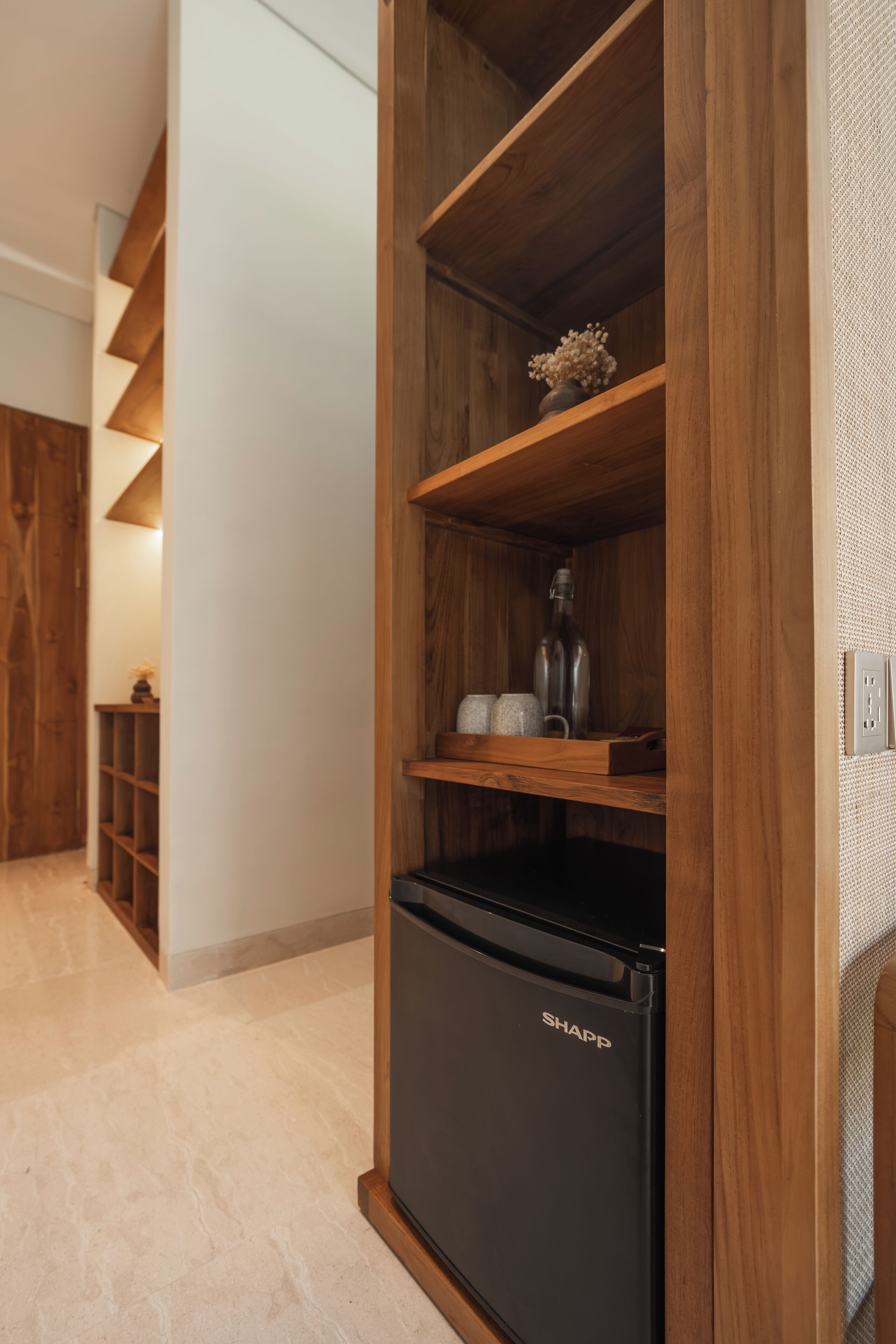 Una cocina con un refrigerador negro, estantes de madera y un florero con flores secas.