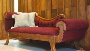 A red upholstered sofa with a white pillow against a wooden wall. - Salty Lotus Hotel (Pecatu)