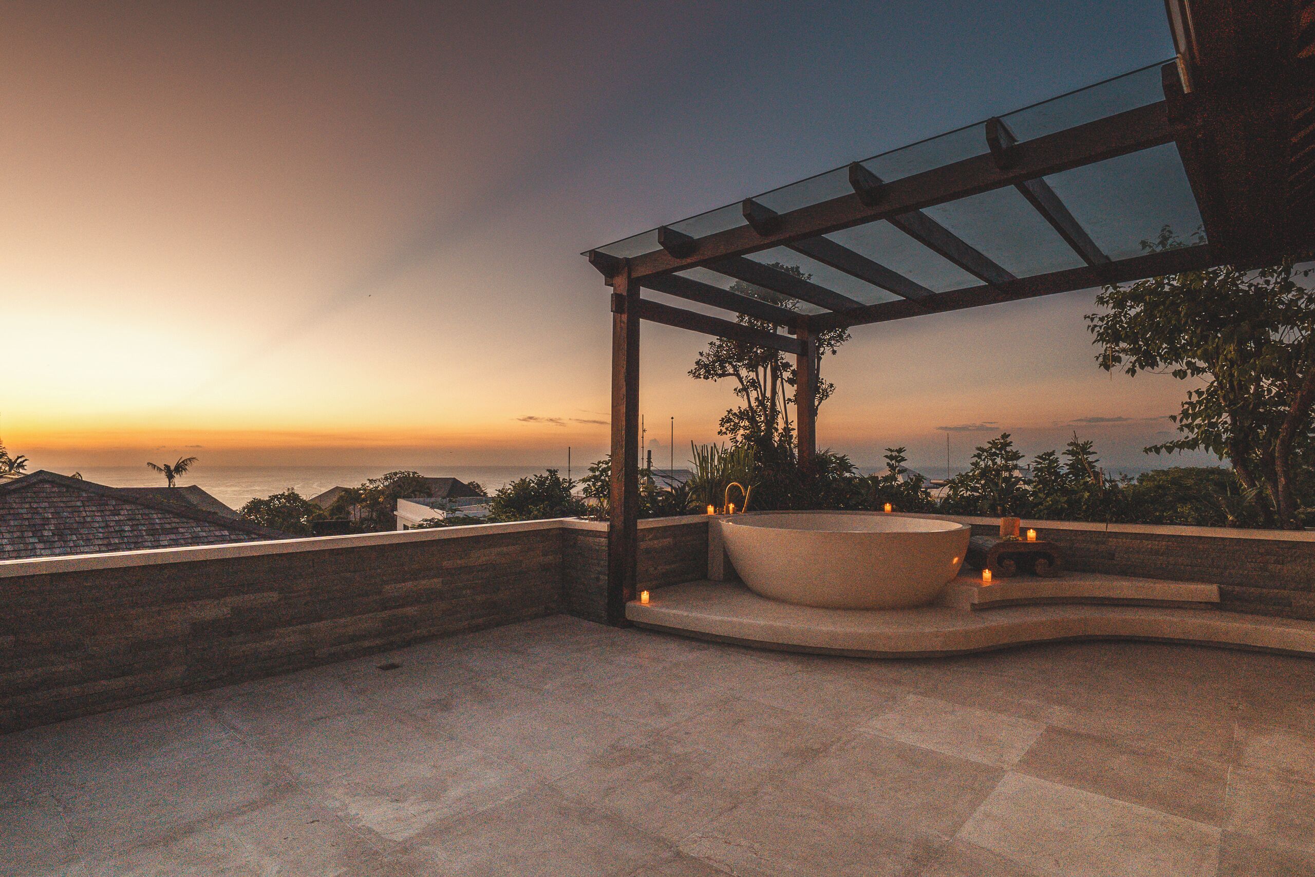 A rooftop terrace with a large bathtub, a pergola, and a view of the ocean at sunset.