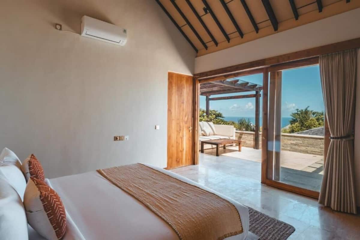 Un dormitorio con una cama, una puerta de madera que da a un balcón y vistas al exterior.