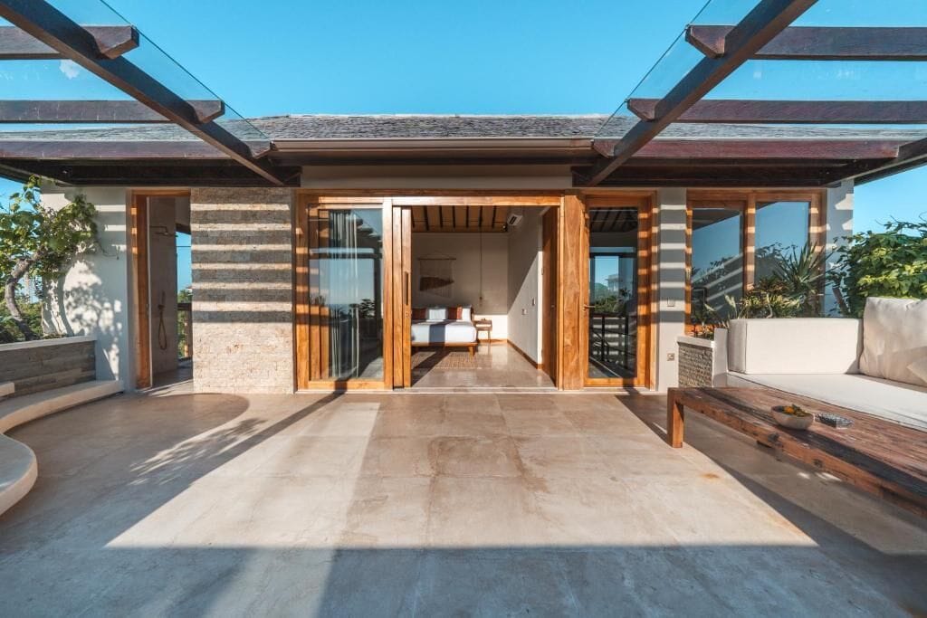 Ein modernes Haus mit einer großzügigen Terrasse, einem sichtbaren Schlafzimmer mit Bett und Fenster sowie einer Holzterrasse.