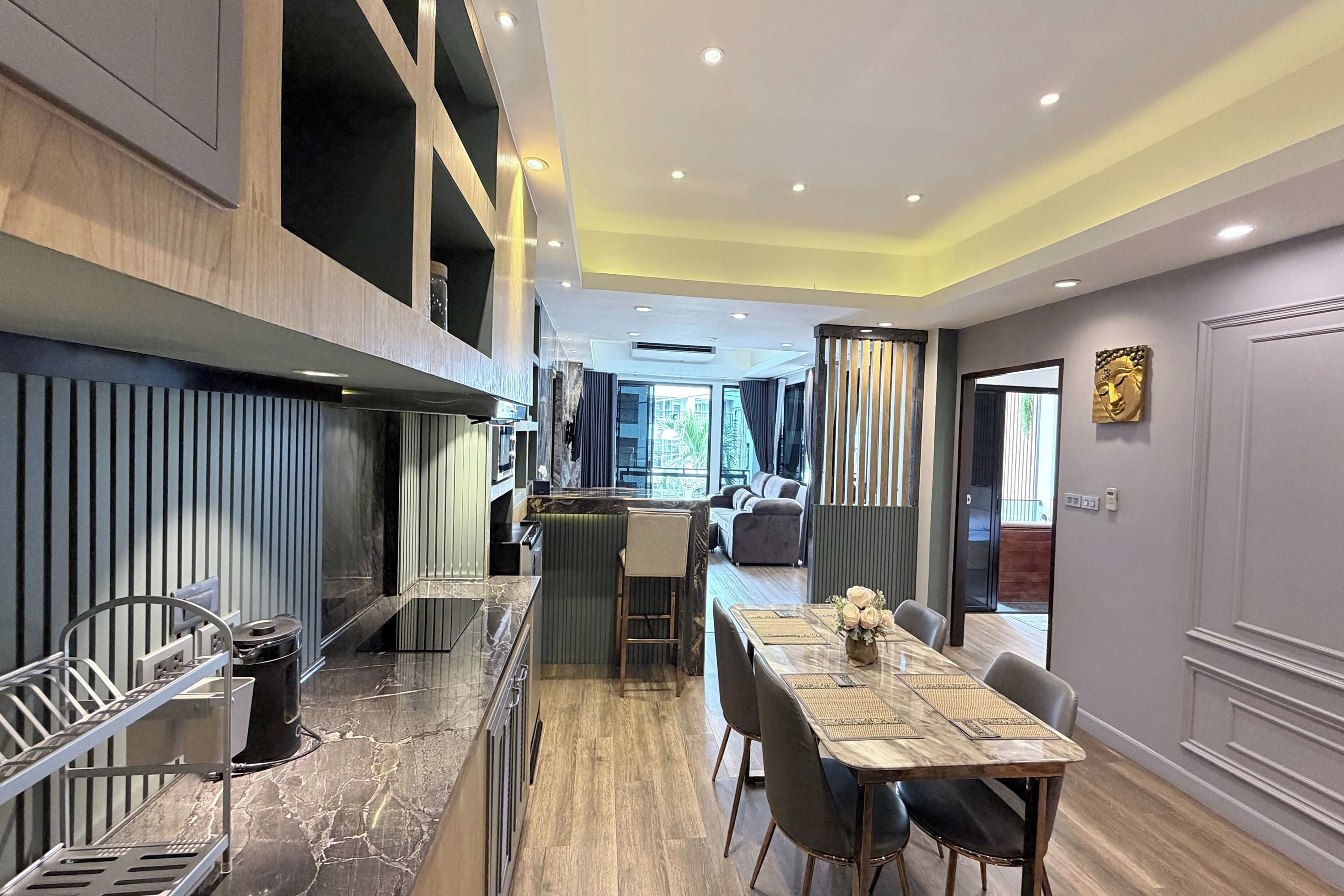 A modern kitchen with a central island, a dining area with a marble table, and a view into the living room.
