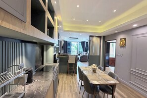A modern kitchen with a central island, a dining area with a marble table, and a view into the living room. - M&M Rooftop Pattaya (Pattaya)
